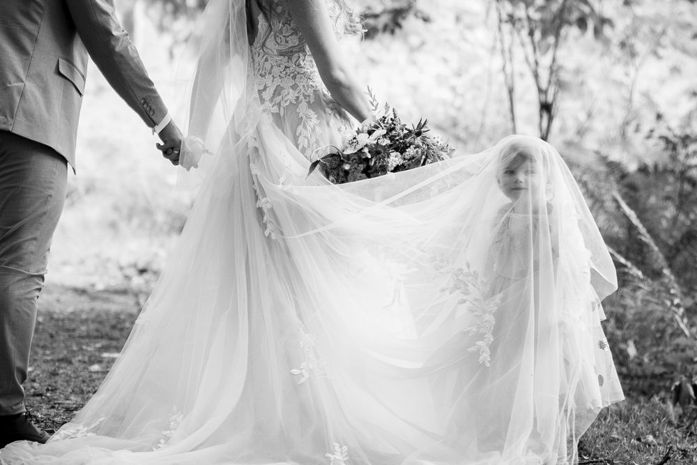 Black and white image of a flowing wedding dress being held up in a garden setting.