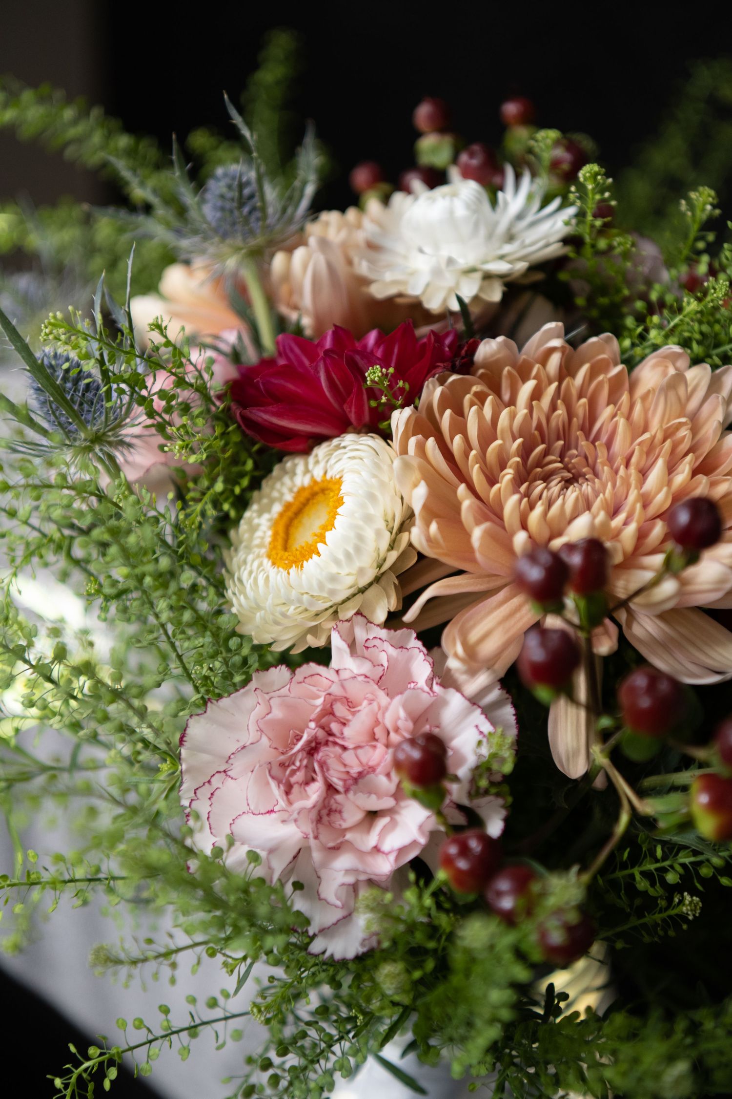 A detailed close-up of a lush floral arrangement featuring chrysanthemums, carnations, and ferns in pink, peach and white tones.