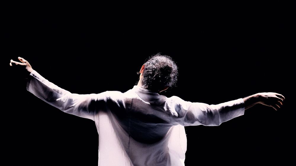 Dramatic silhouette of performer with outstretched arms against black background.