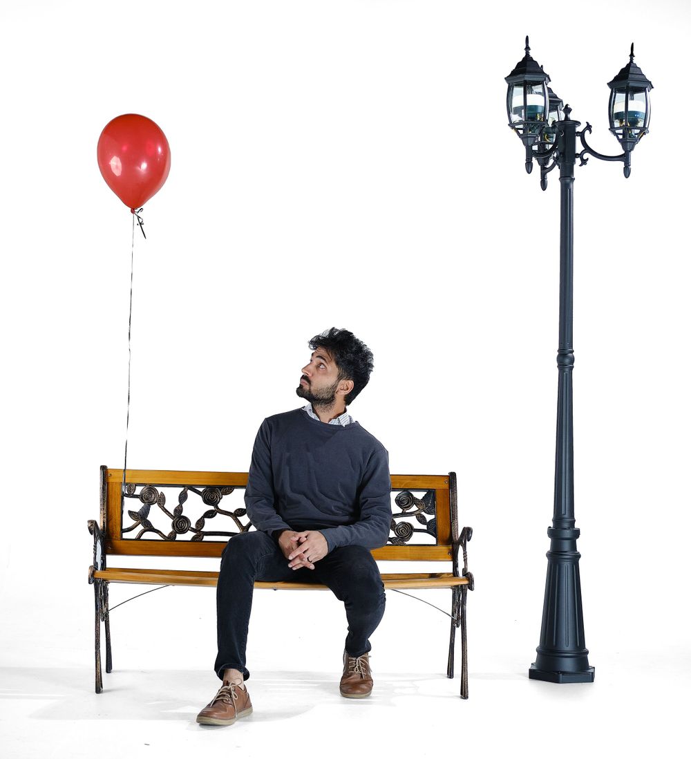 Artistic portrait with red balloon, vintage lamp post, and wooden bench against white background.