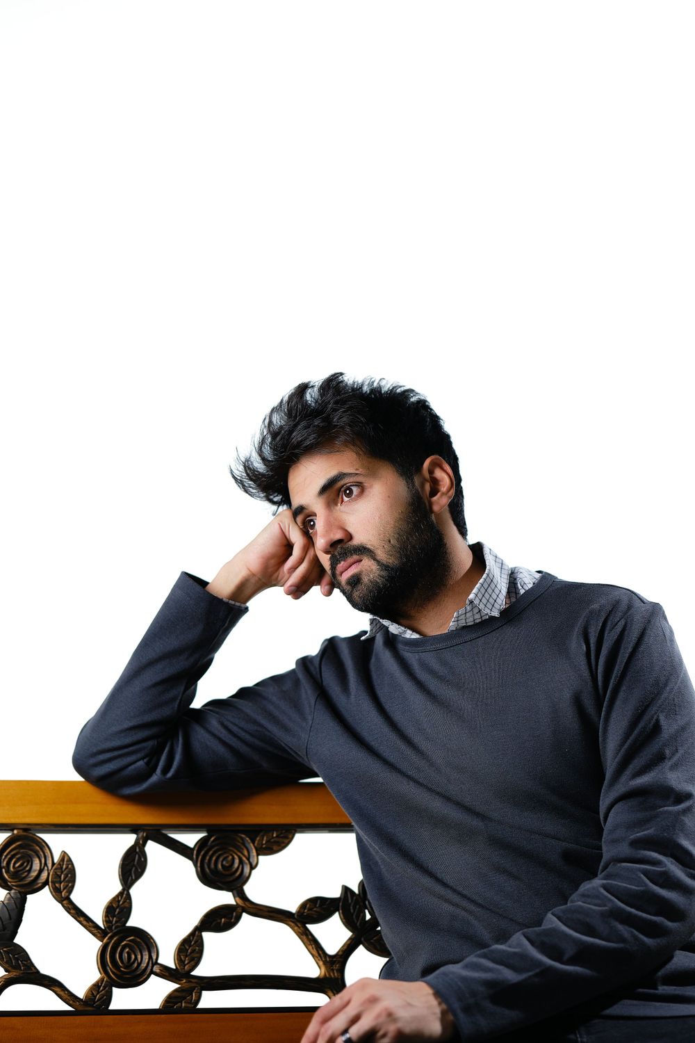 Person in navy sweater leans thoughtfully against ornate railing in contemplative portrait pose.