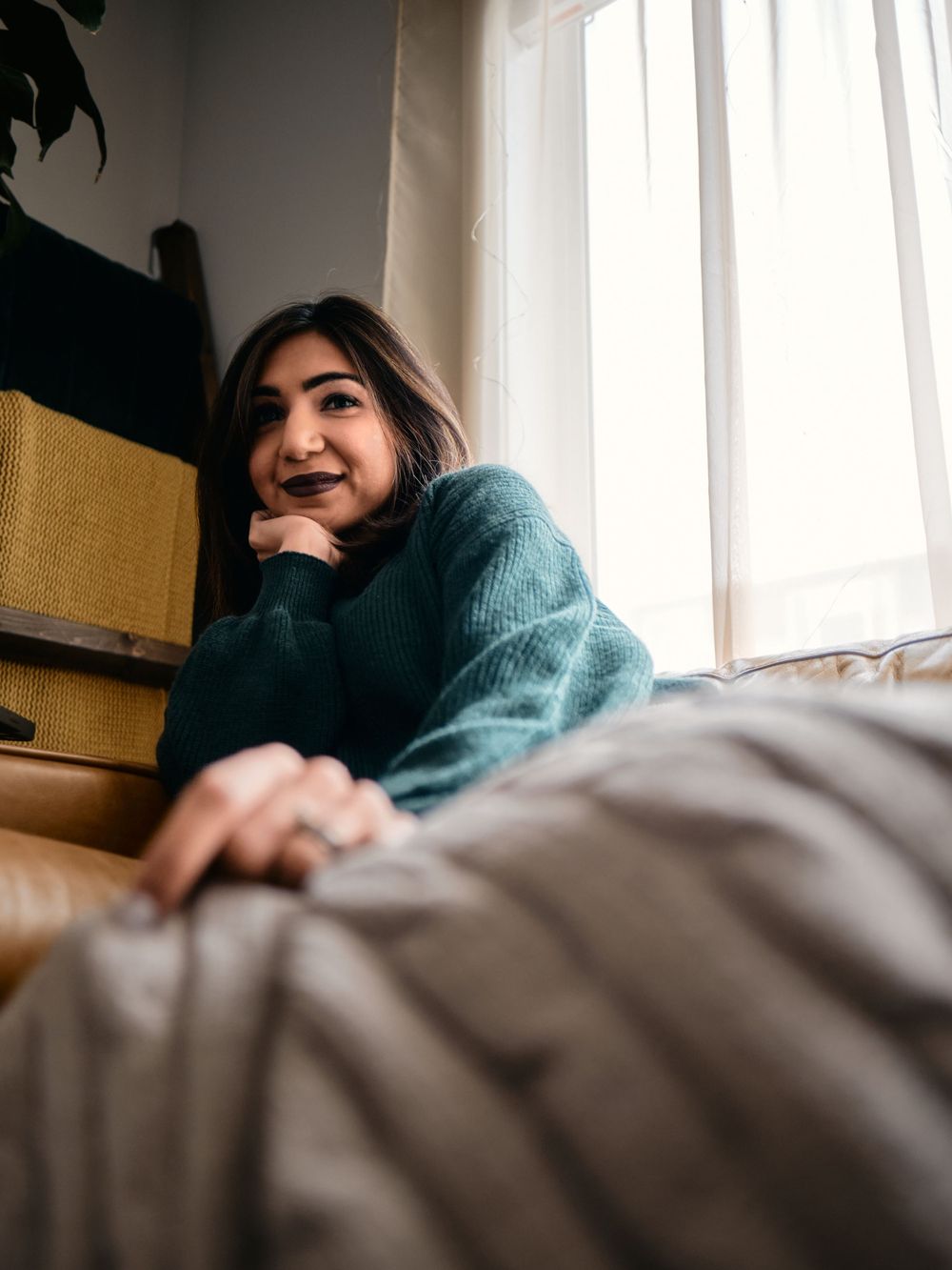 Portrait of a model wearing a cozy sweater relaxing by a window in a warm, sunlit room with casual home decor.