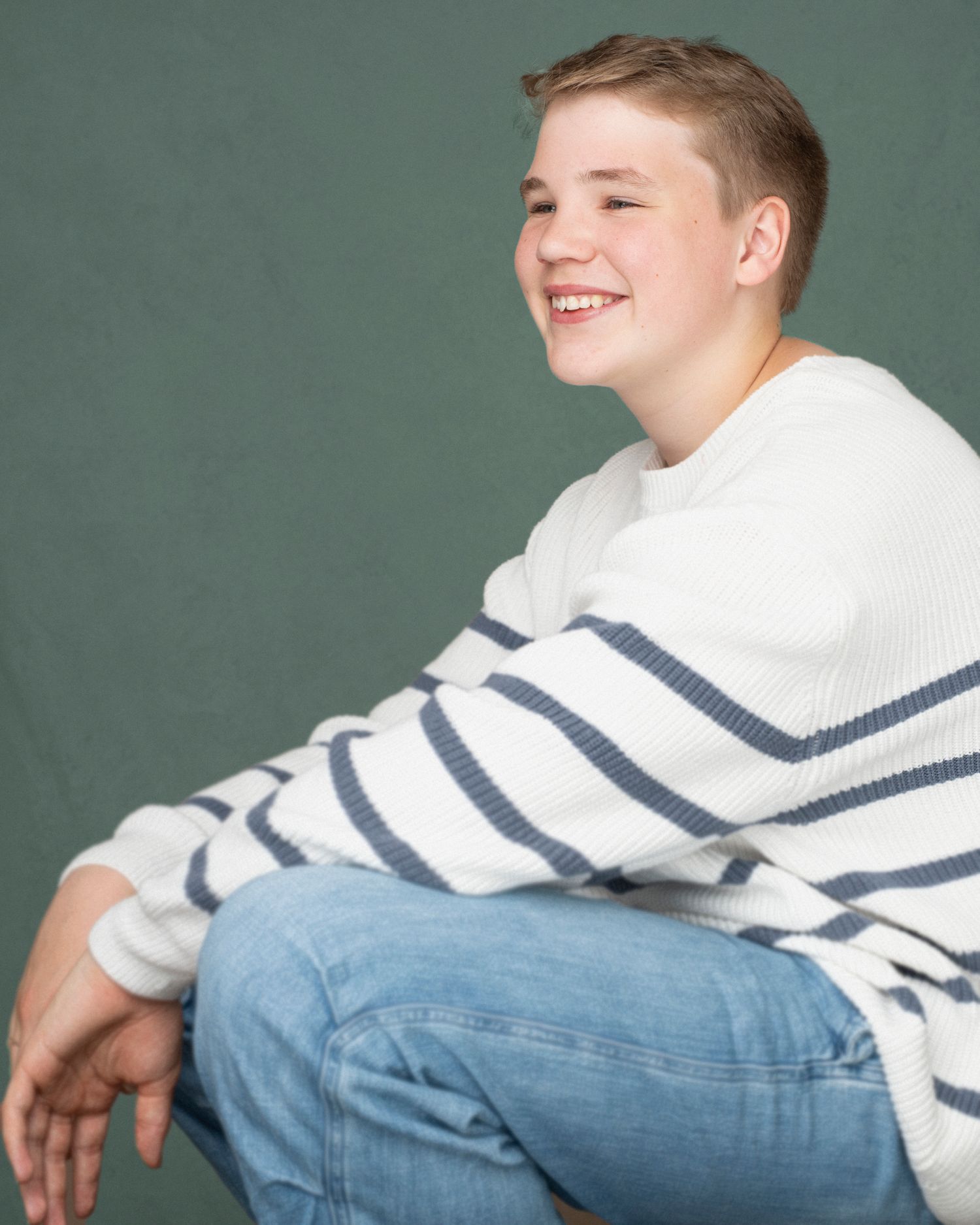Casual portrait of someone in striped sweater and jeans against green background.