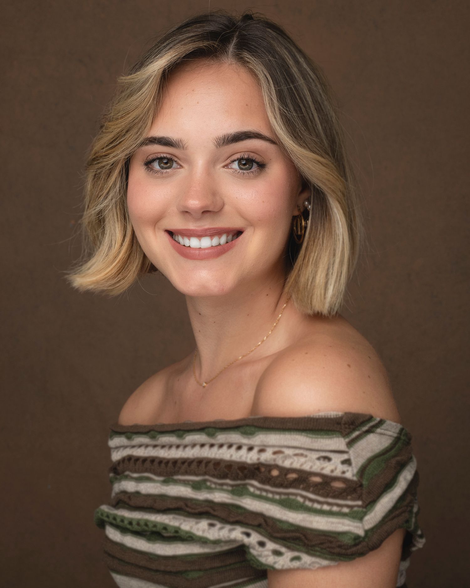 Professional studio portrait against brown background featuring off-shoulder striped top.