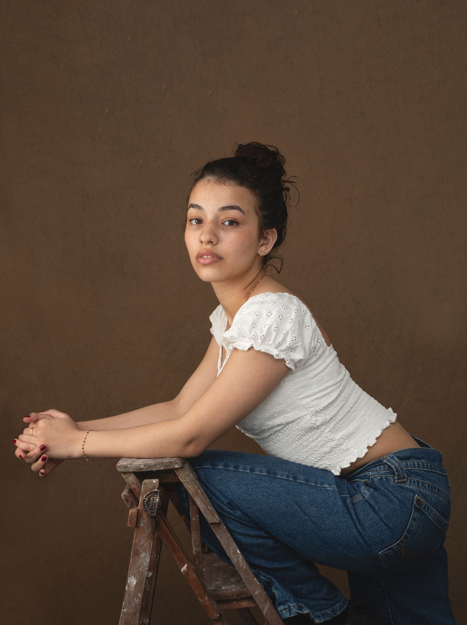 Casual portrait of someone sitting on wooden steps wearing jeans and white top.
