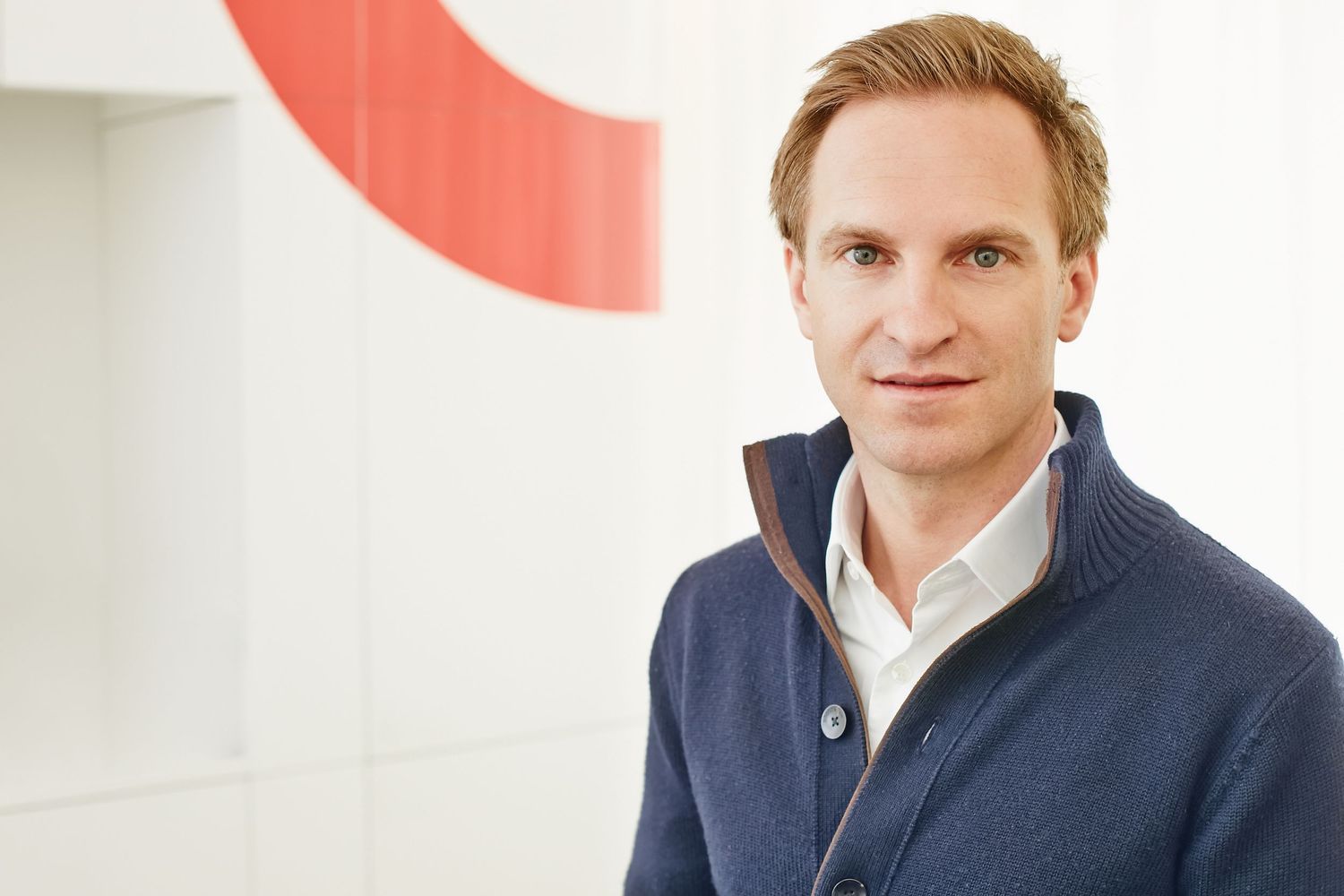 Professional man in a navy sweater posing confidently in a modern office.