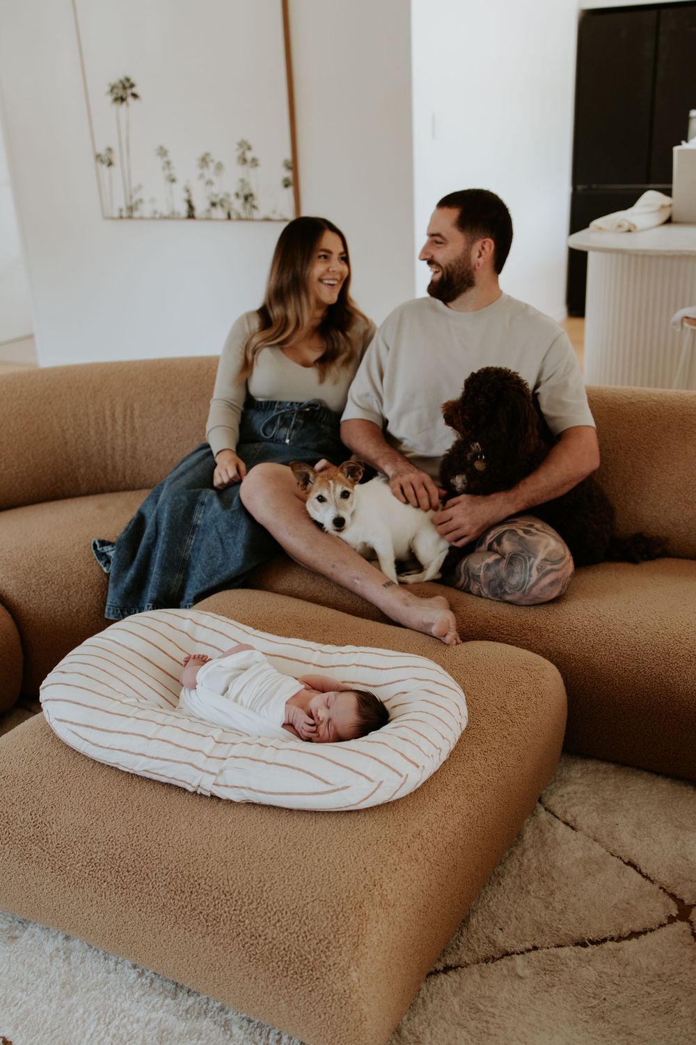 A couple relaxes on a brown couch with their dogs while enjoying a cozy moment at home.