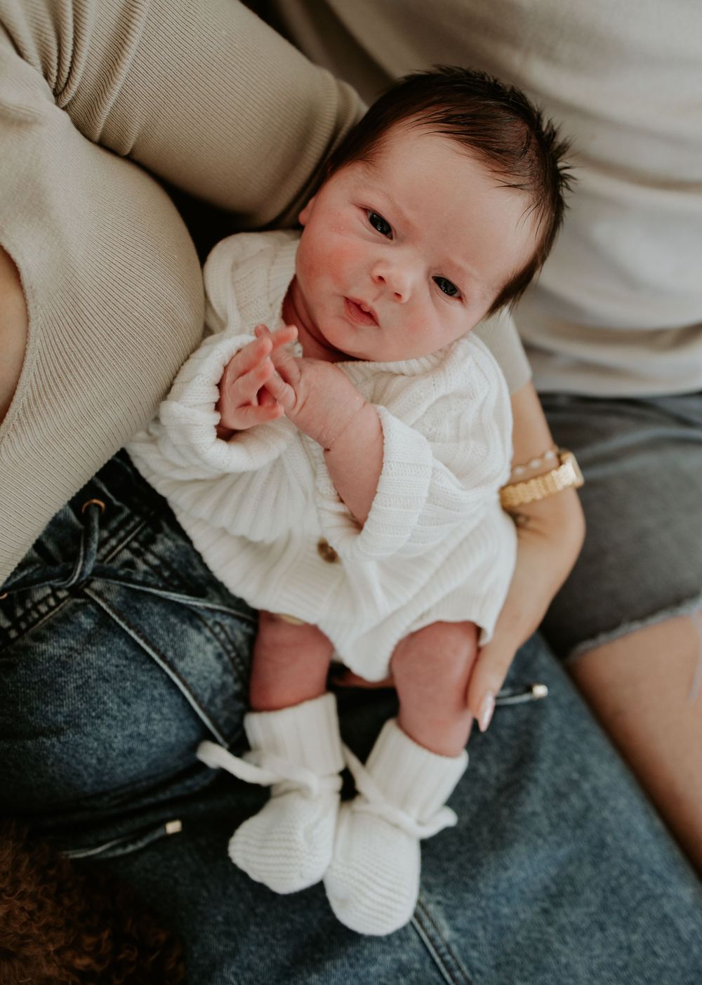 Baby wearing white top lies on parent's lap with denim jeans in series of candid lifestyle photos.