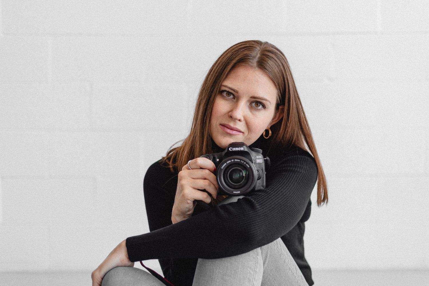 Casual photographer sitting with camera against white studio background.