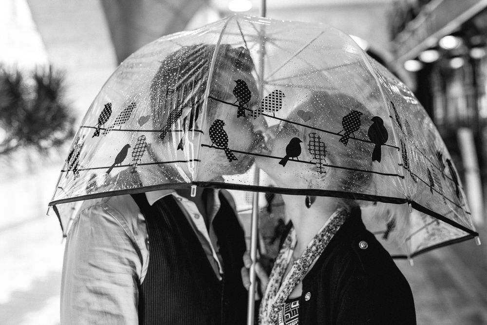 Two people share an umbrella while walking together in a romantic black and white photo.