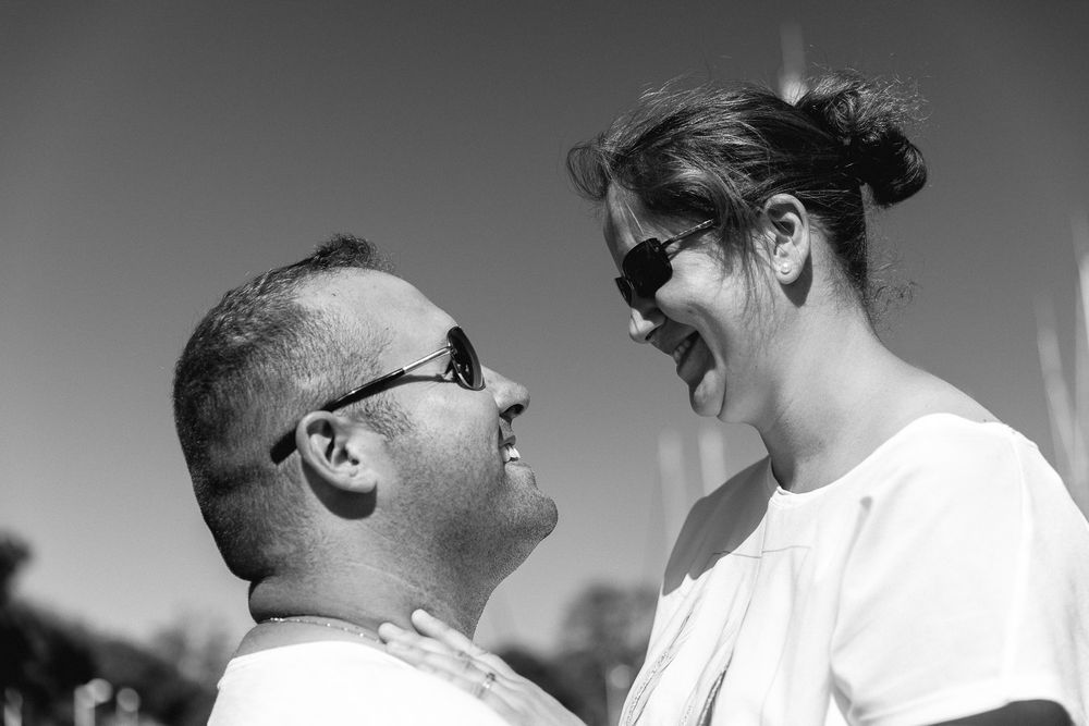 Black and white photo showing two people laughing joyfully together outdoors in bright sunlight.