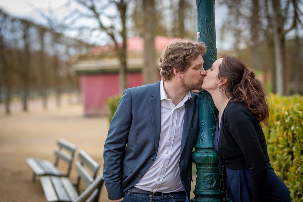 A romantic couple sharing a tender moment while leaning against a green lamp post in a park setting.