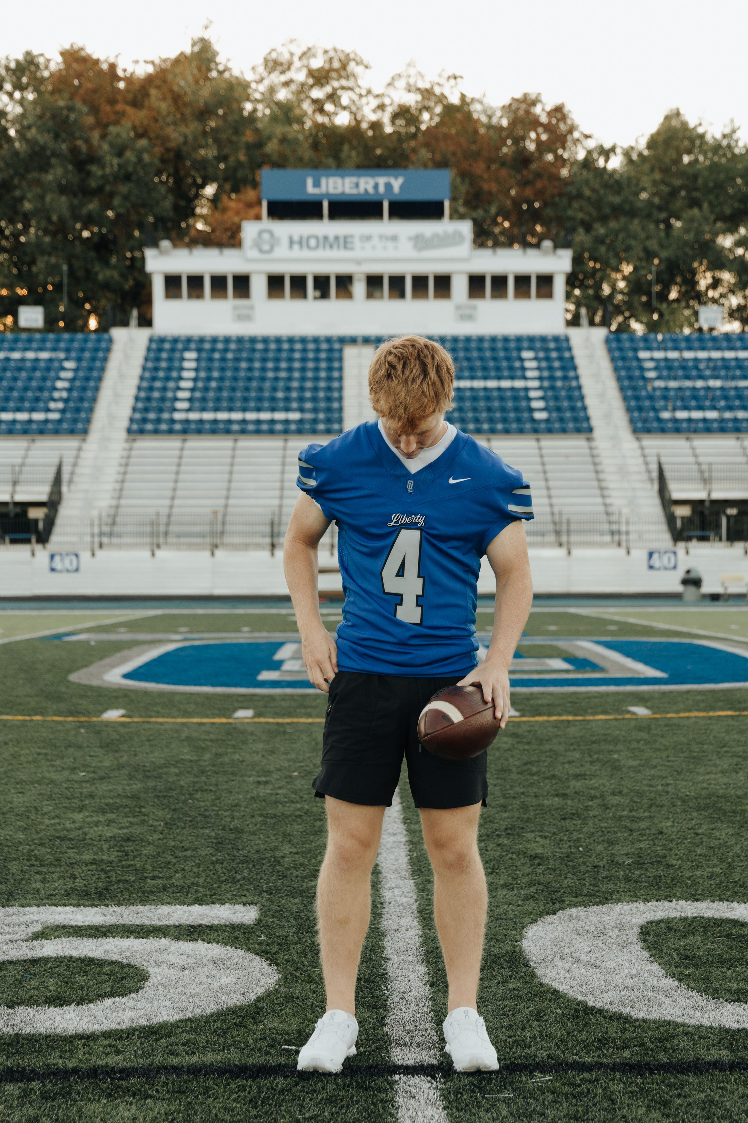 High school senior posing in his football jersey on Liberty high school’s field.