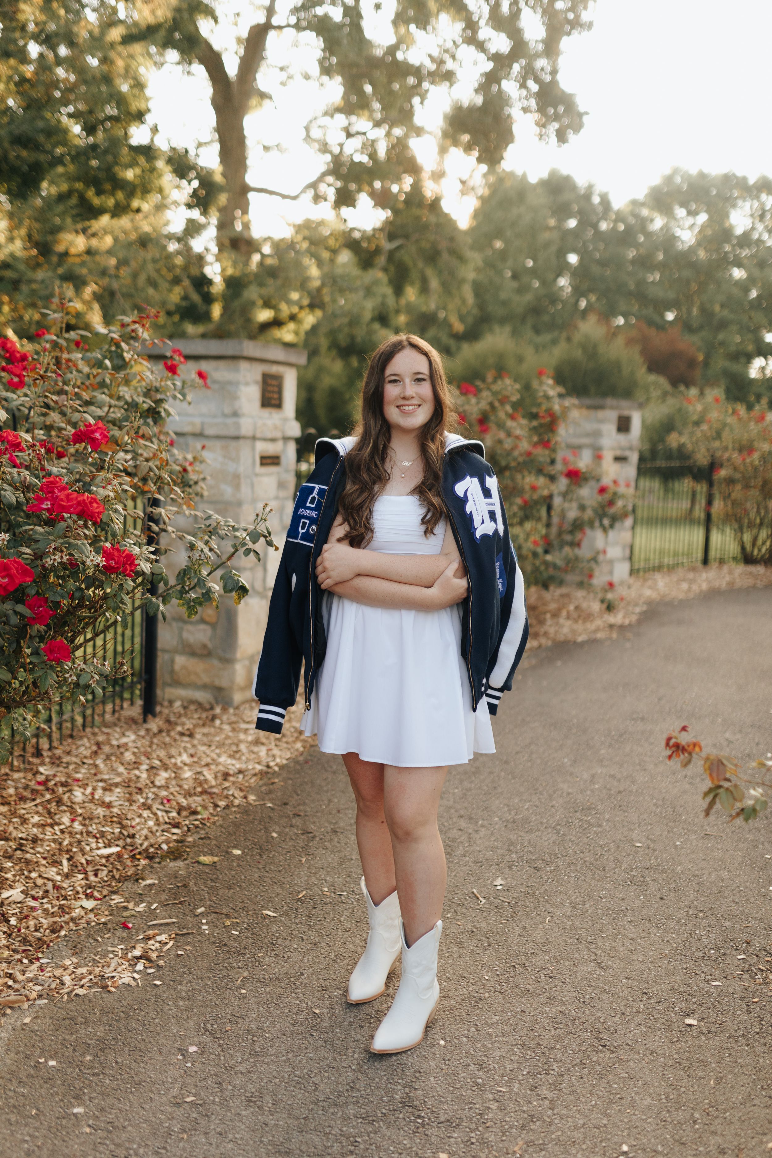 Young senior wearing letterman jacket and dress in park full of flowers.