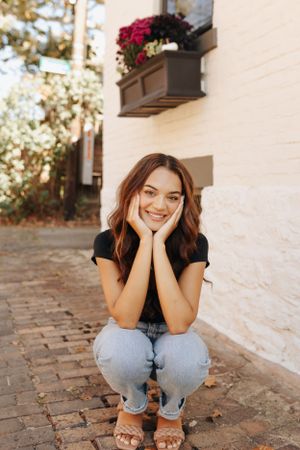 High school senior smiling in downtown village, with brick-lined streets and cute buildings.