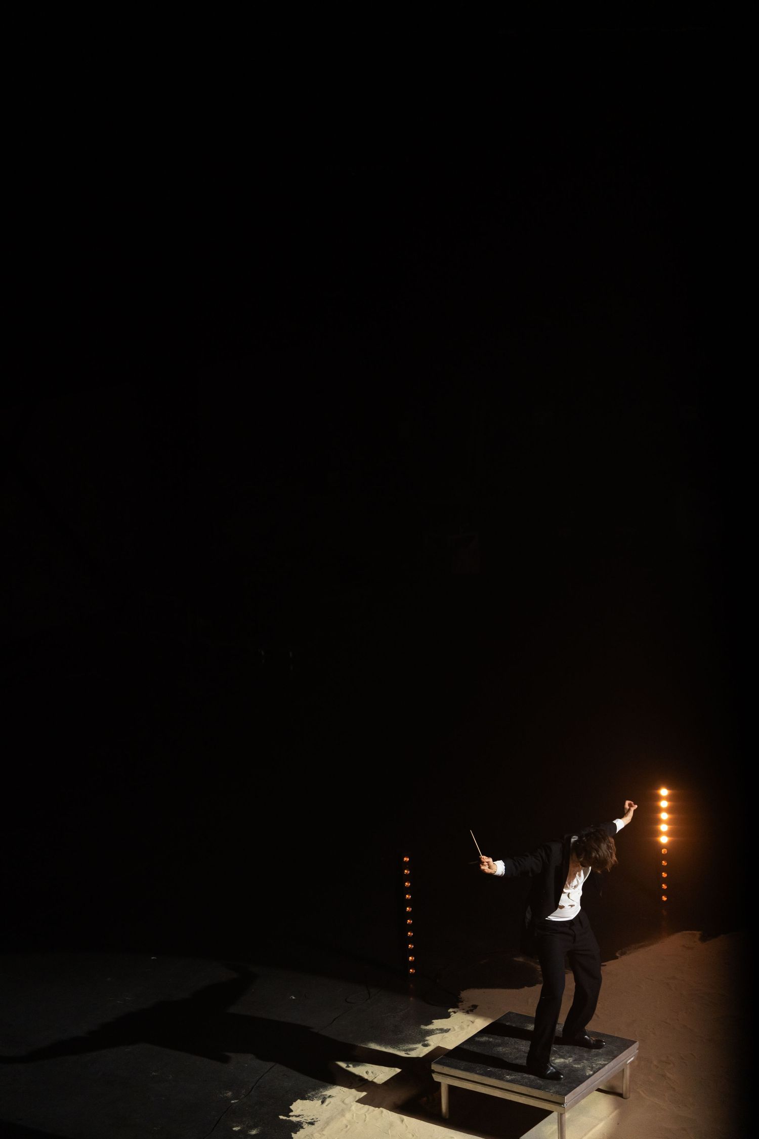 Silhouette of performer on elevated platform against dark background with stage lights.