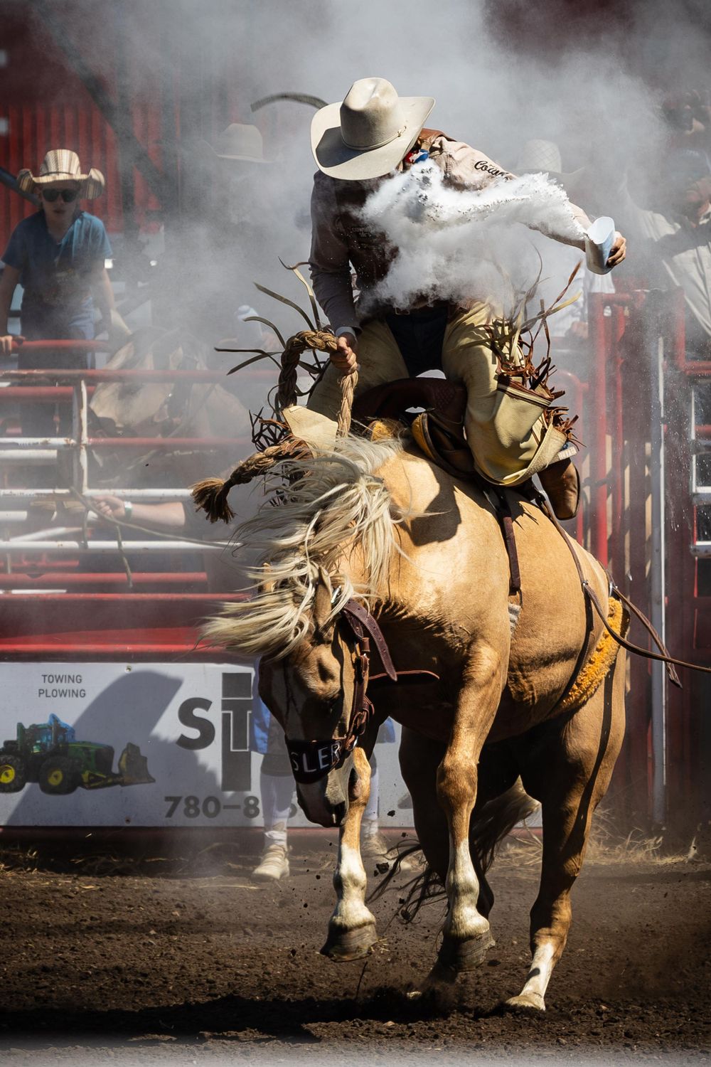 Rodeo rider on bucking bronco kicks up dust during intense competition.