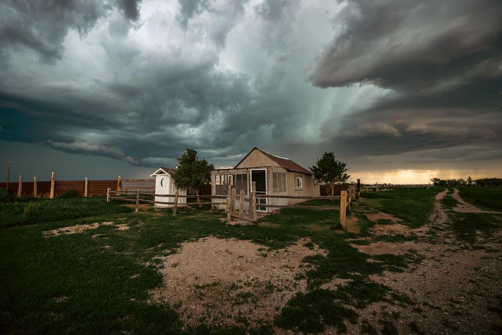 Storm clouds gathering over rural houses on plains with dramatic lighting.