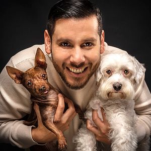 Two dogs, one brown and one white, pose with owner against dark backdrop.