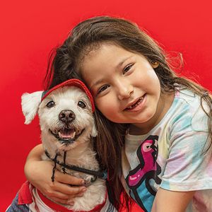 Small white dog with Santa hat poses against red background.