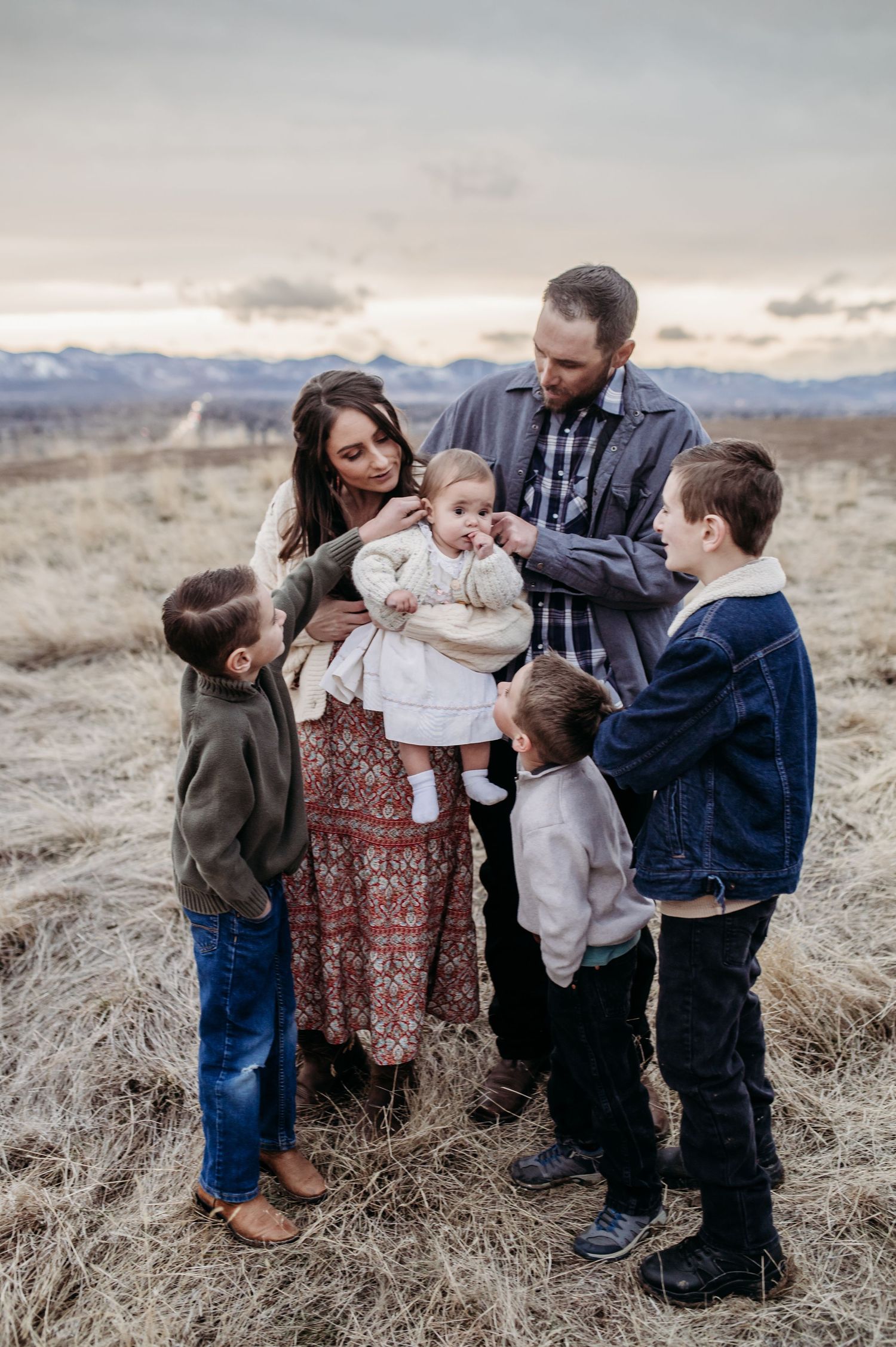 Family standing in a Colorado field at sunset with mountains in the background.