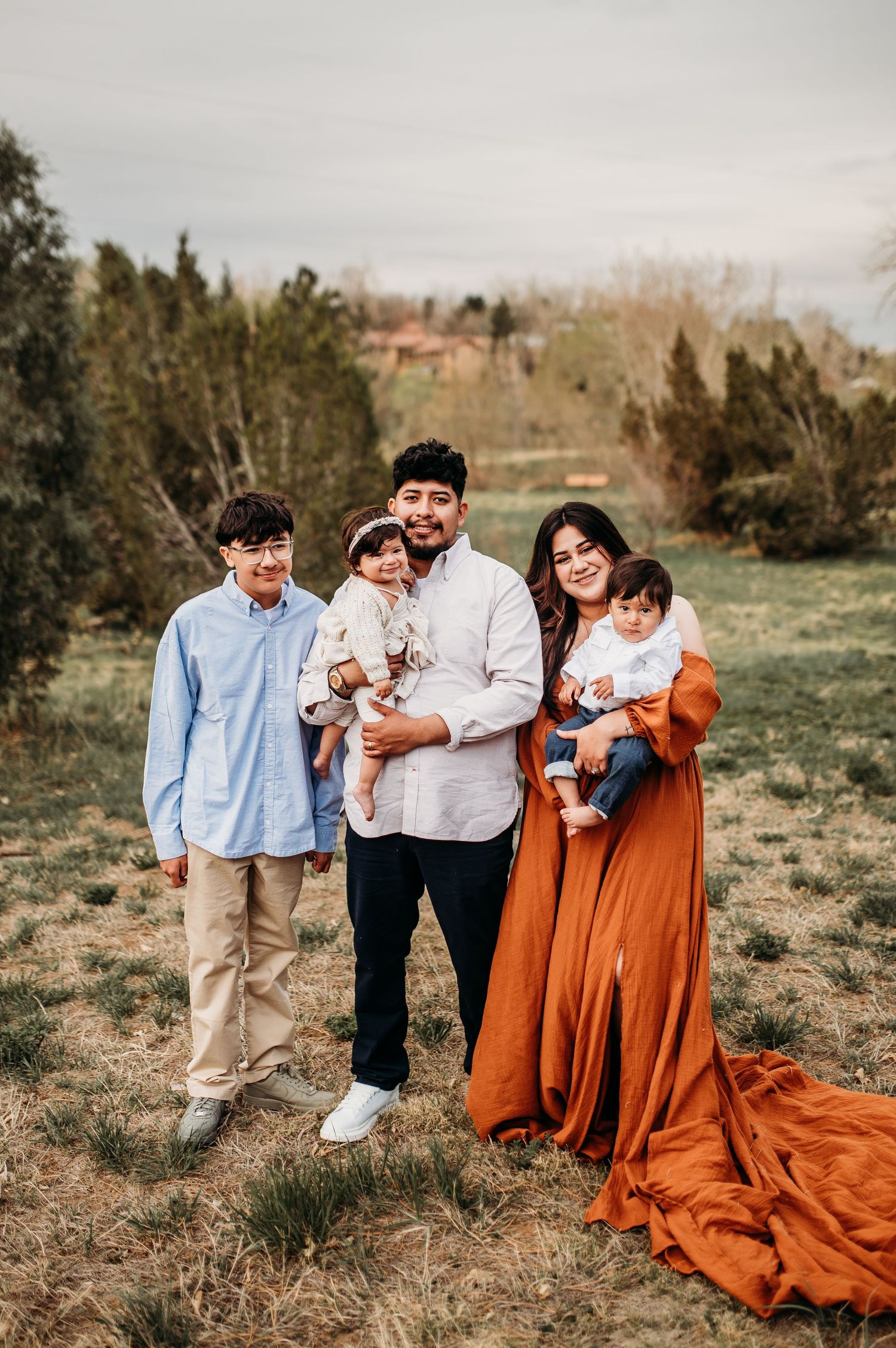 Family of five walking outdoors in a grassy field with cloudy skies.