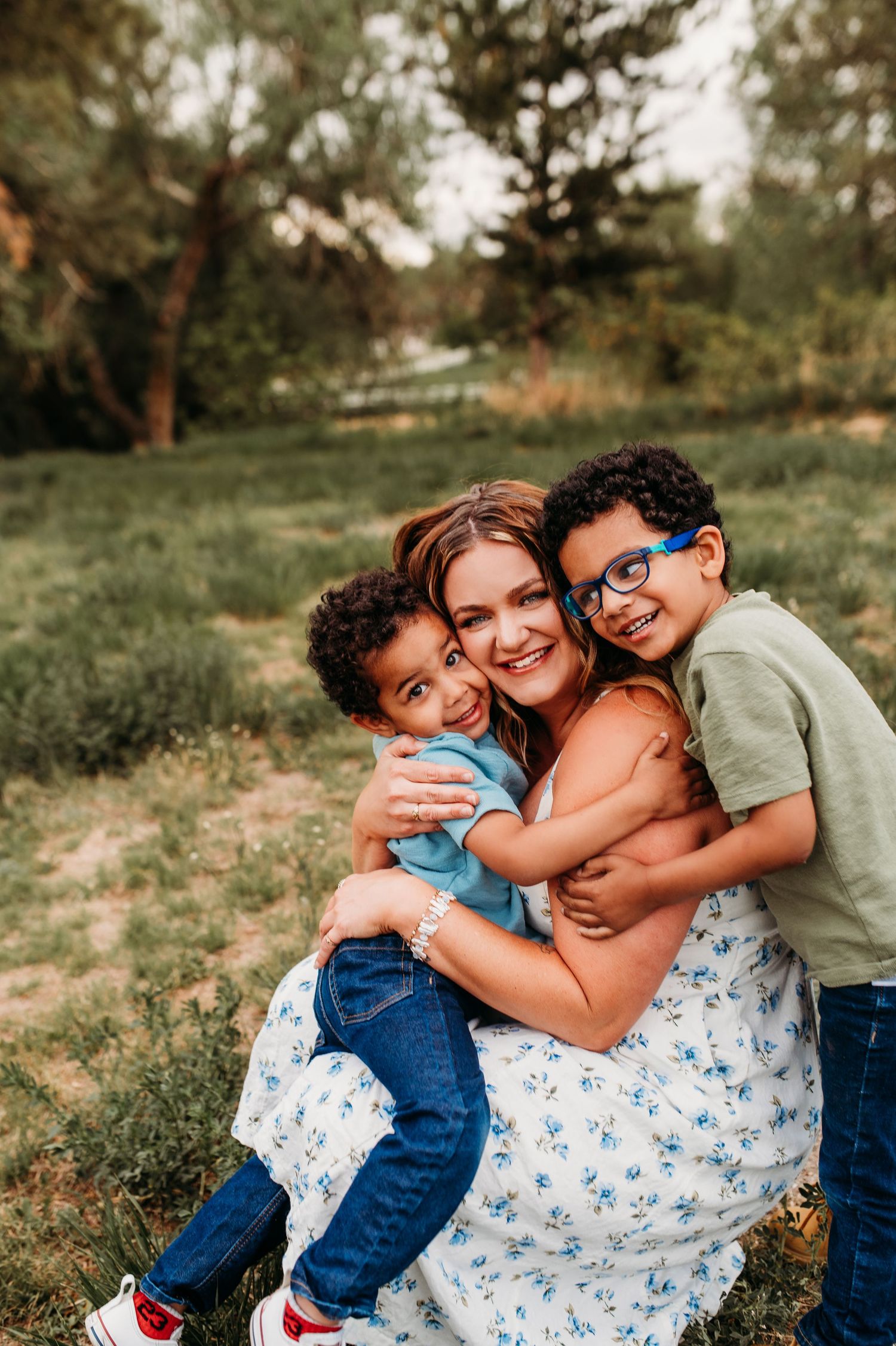 Mother hugging two young children in a green field during summer