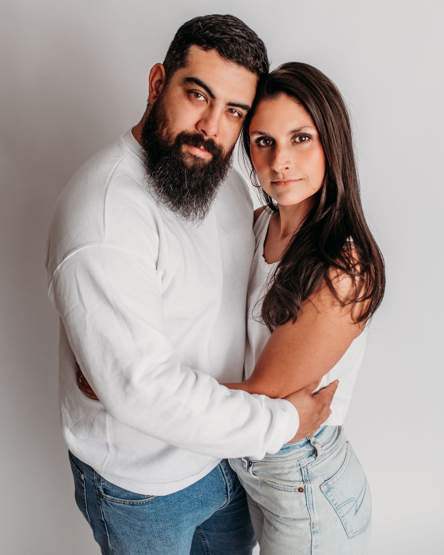 Studio portrait of a couple in white clothing, embracing against a gray background