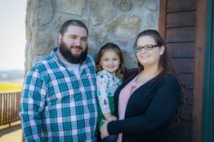 Family of three poses together on a rustic stone porch.
