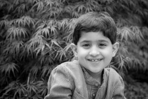 Black and white portrait of a smiling child against foliage background.