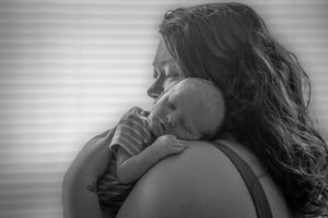 A tender black and white portrait of a parent cradling a sleeping newborn baby against their shoulder.