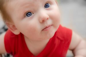 Close up portrait of a baby in a red outfit with bright blue eyes looking at the camera.