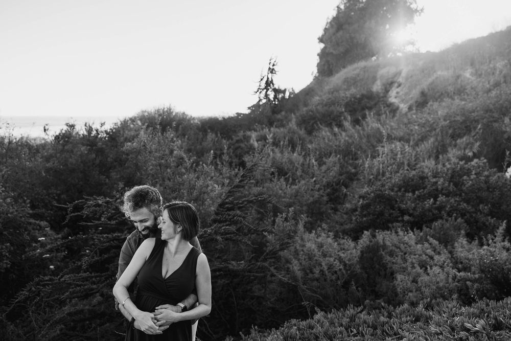 A person stands on a mountain trail overlooking a scenic valley in black and white.
