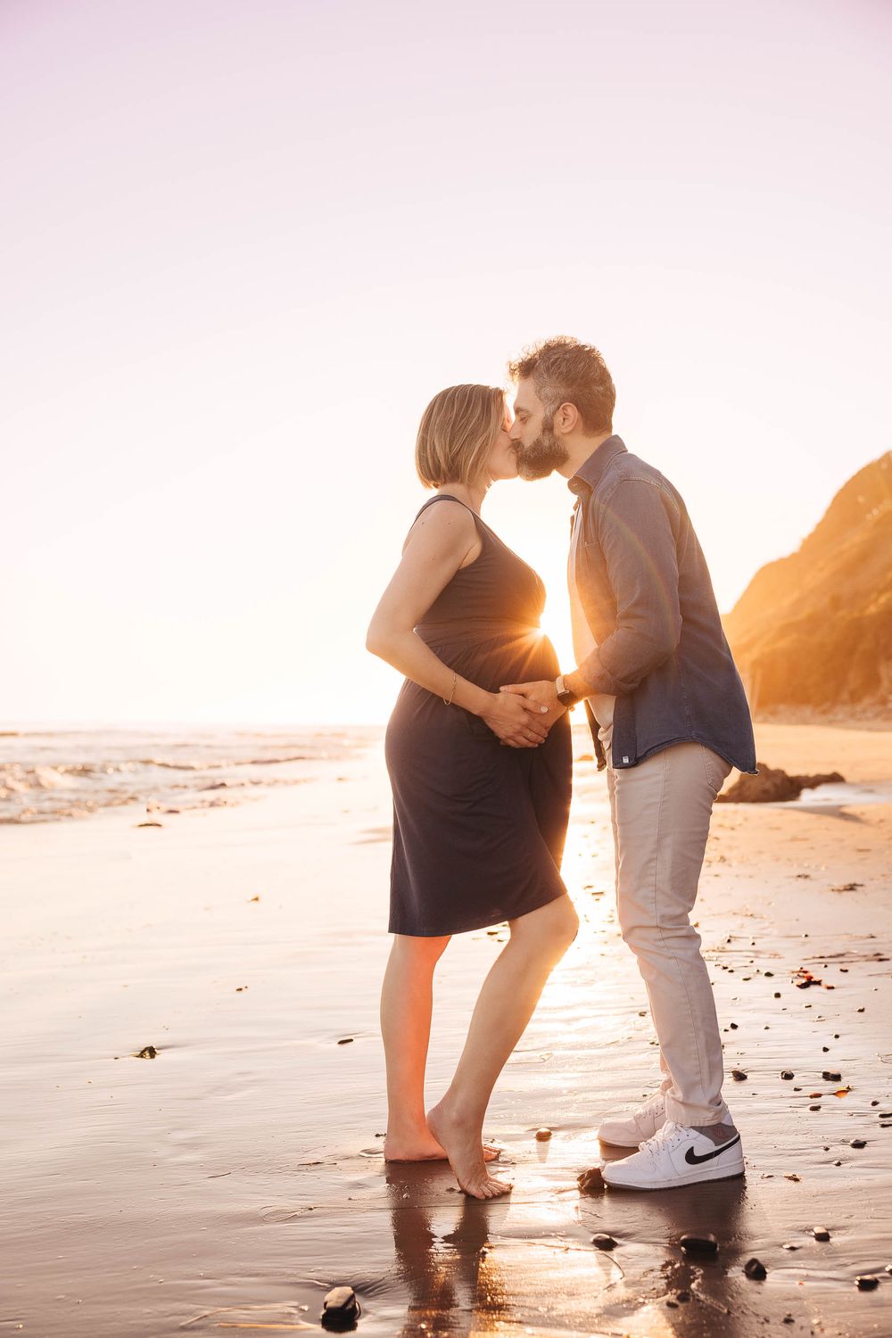 Romantic couple sharing an intimate moment on a sunset beach with cliffs in the background.