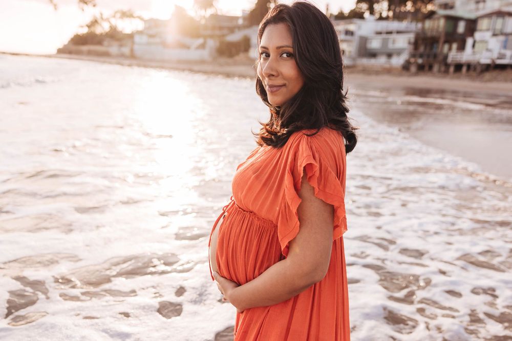 Person in a flowing orange dress poses gracefully on a sandy beach at sunset.