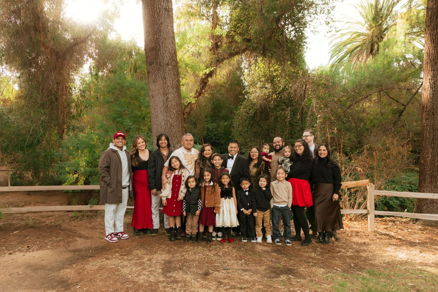Large group portrait of people standing together on a wooden platform in a wooded outdoor setting during golden hour.