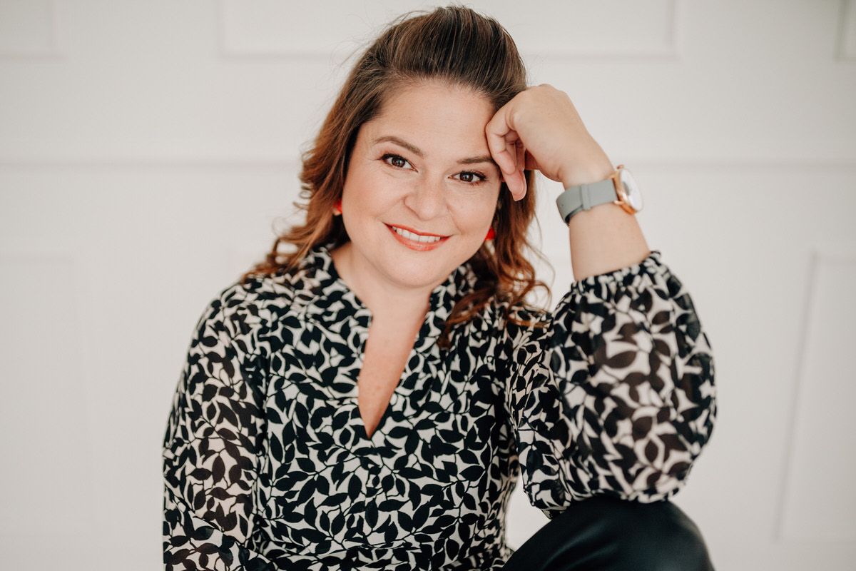 Professional headshot of woman in white blouse with warm smile against light background.