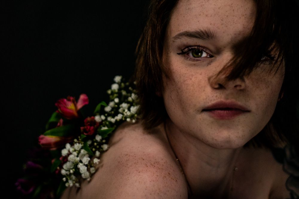 Artistic portrait against dark background with red flowers and baby's breath floral elements.