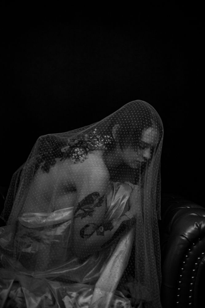 Moody black and white portrait through delicate lace veil against dark background.