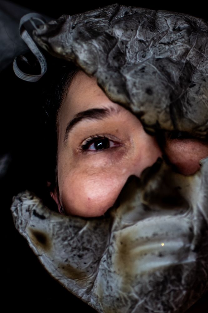 Close up artistic photo showing eyes peering through wisps of gray smoke against a dark background.