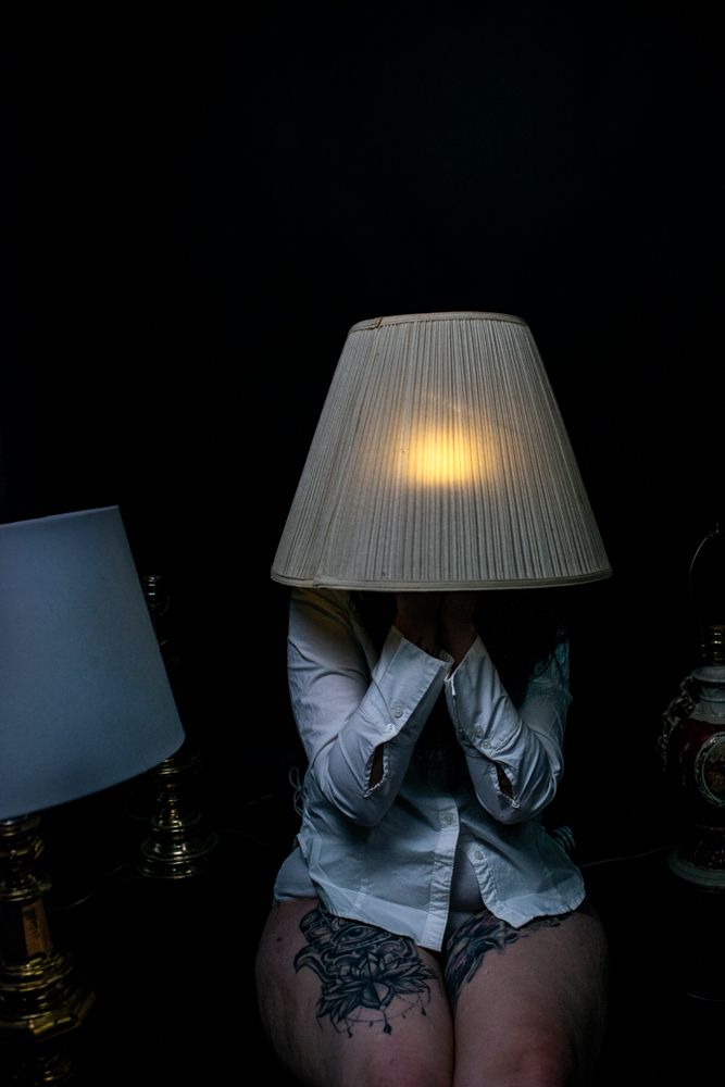 An artistic photo of illuminated lampshades in darkness with shadowy figure beneath.