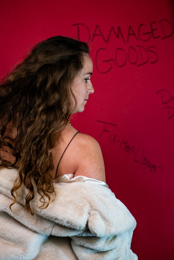 Profile view of figure in off-shoulder white sweater against red wall with graffiti text.