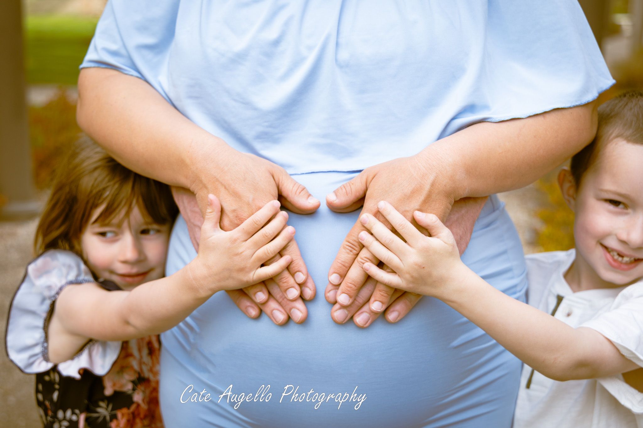 Little ones embrace a person wearing light blue clothing while holding their hands in Maternity photo session South Windsor, CT