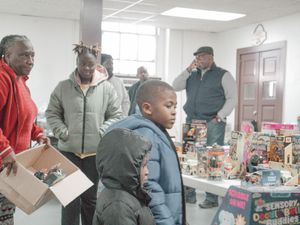 People browse toys and collectibles at an indoor holiday sale or flea market event with display tables.