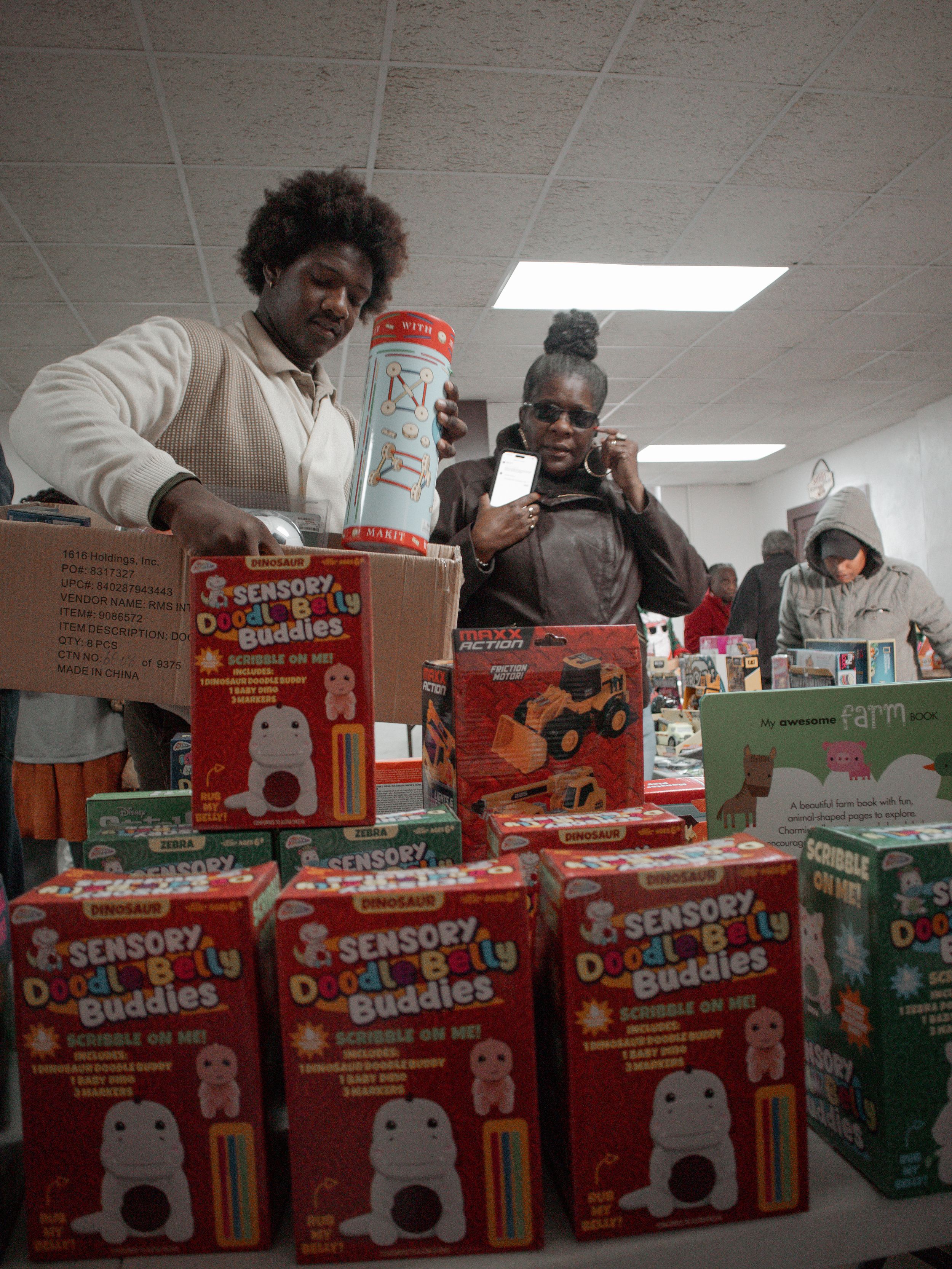 Multiple boxes of Snoopy Sno-Cone making machines stacked on a table while people examine them at an indoor location.