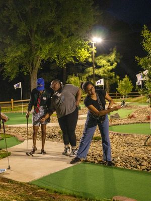 People enjoying a round of mini golf at night on an illuminated course with trees and pathways.