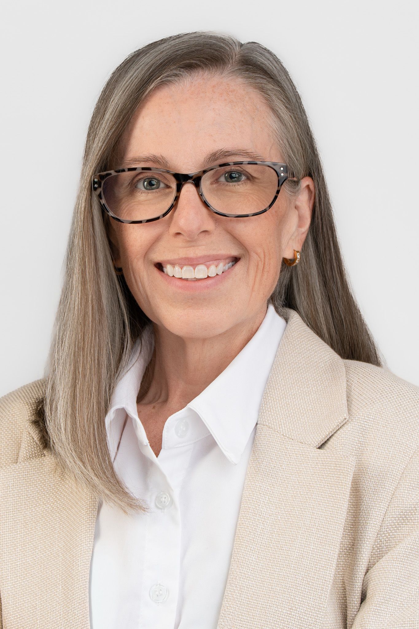 Professional woman with gray hair, glasses, and a beige blazer smiling confidently against a white background.