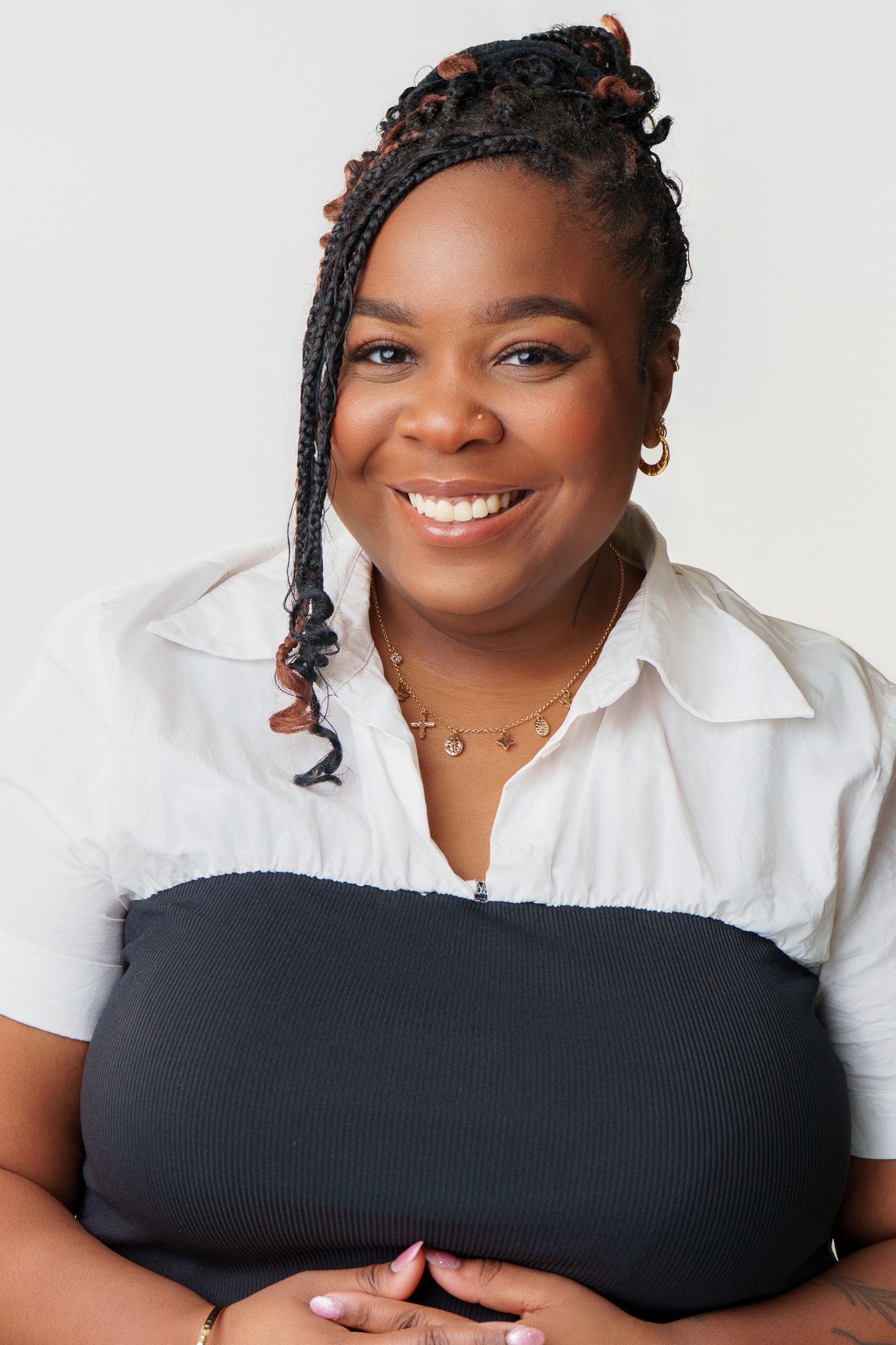 Smiling Black woman with braided hair wearing a white shirt and black top, posing confidently against a light background.