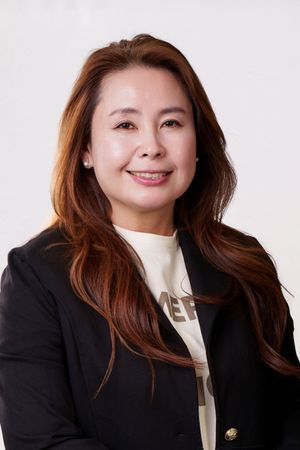 Professional headshot of a smiling Asian woman with auburn hair, wearing a black blazer over a casual top.