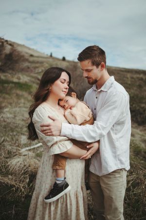 A family shares an intimate moment together on a hillside during an outdoor portrait session in muted earth tones.